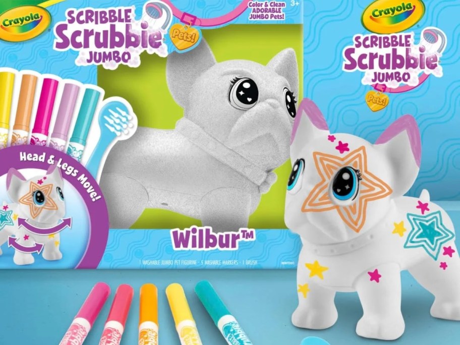 a white toy dog with doodles and drawings on it, Crayola markers laying beside it and the box the toy set onlinees in 