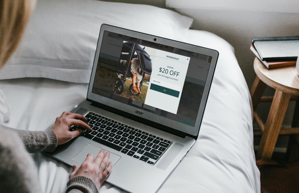 woman typing on laptop sitting on bed with wonderfold wagon coupon on screen