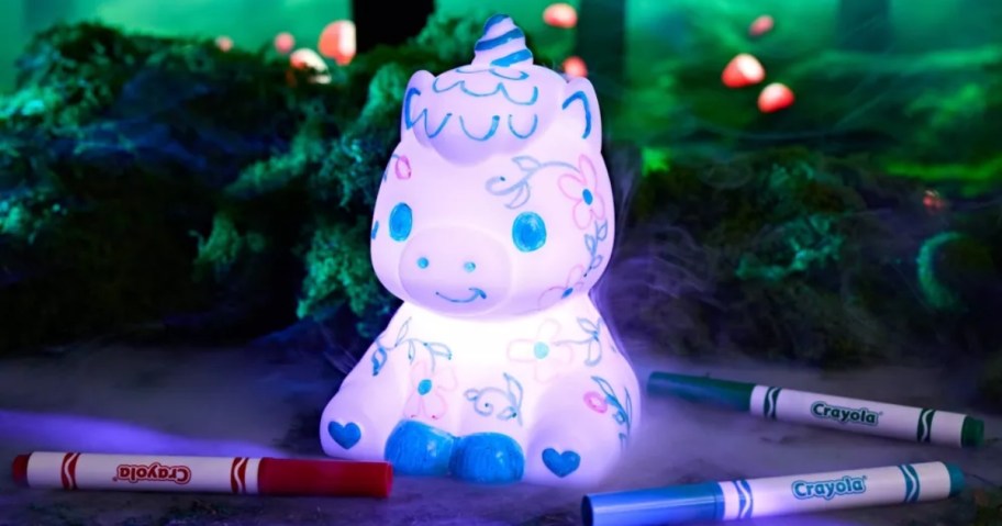 a light up unicorn with doodles on it, Crayola markers laying around it