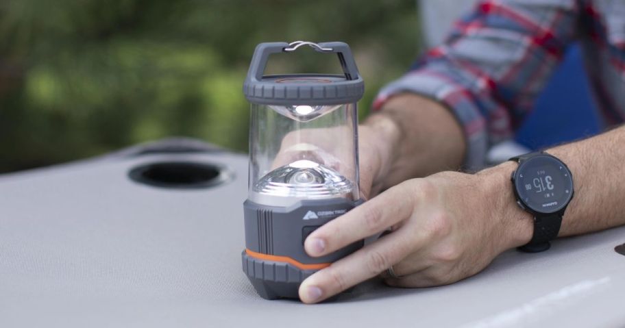 hands holding Ozark Trail 200 Lumen LED Battery Powered Lantern on table