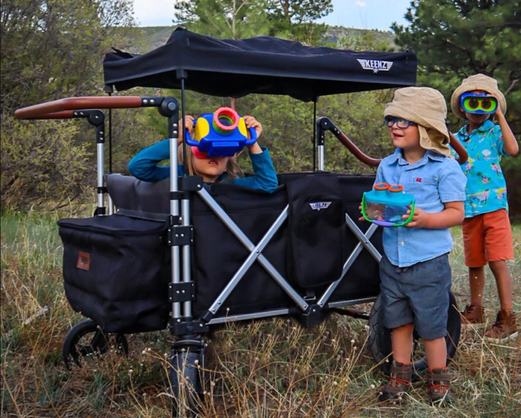 kids outside in grass standing next to keenz stroller wagon