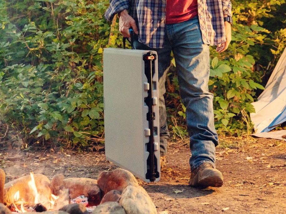person carrying lifetime folding table folded in half through campsite