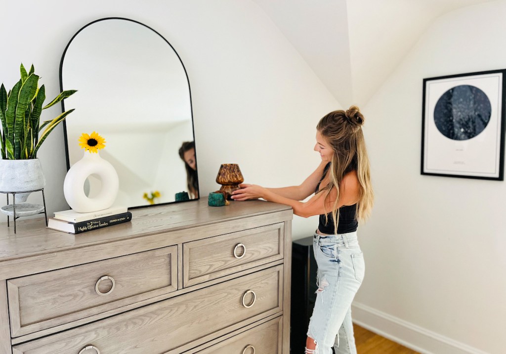 woman holding brown lamp on top of dresser with mirror