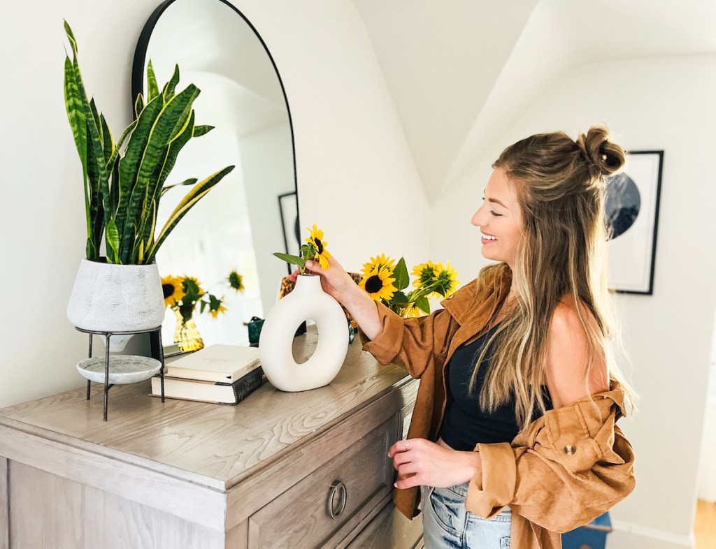 woman putting sunflower in circular matte white vase