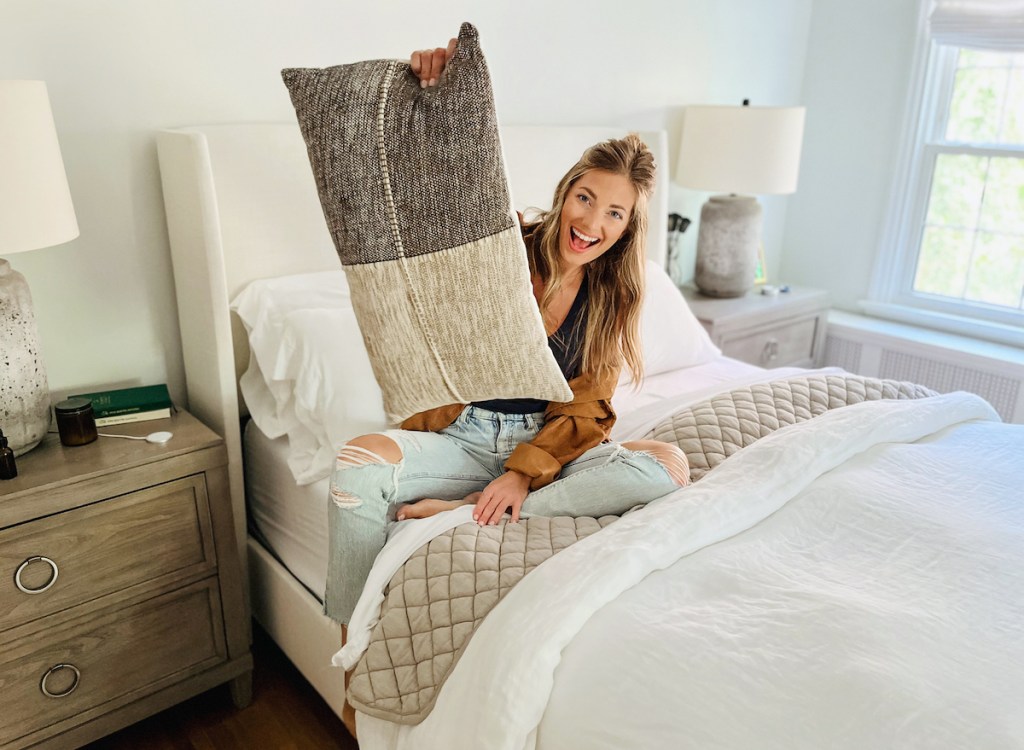 woman sitting on bed holding up throw pillow 