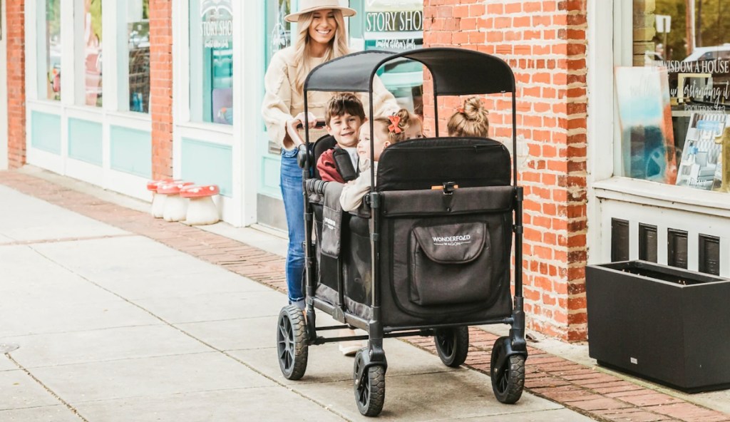 woman walking on sidewalk pushing wagon full of kids