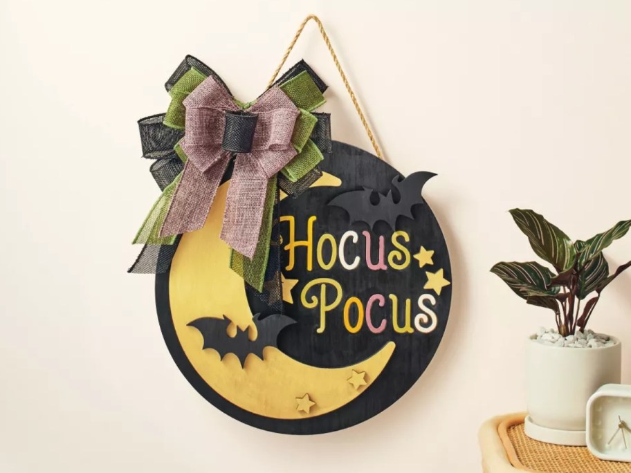 a Halloween wall decor piece with a moon, bat, ribbon that says "Hocus Pocus"