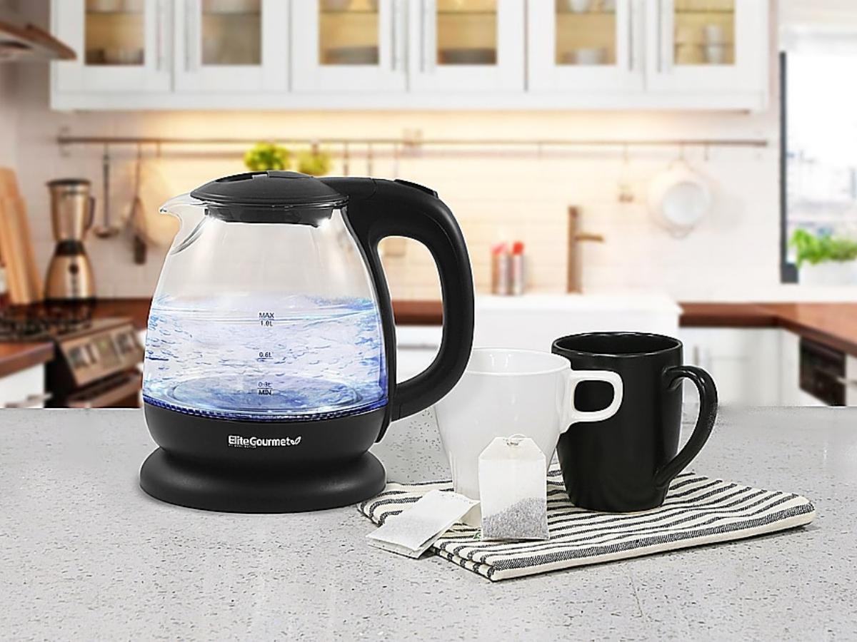 Elite Gourmet Electric Kettle on a table in a kitchen near mugs, tea bags, and a kitchen dish towel