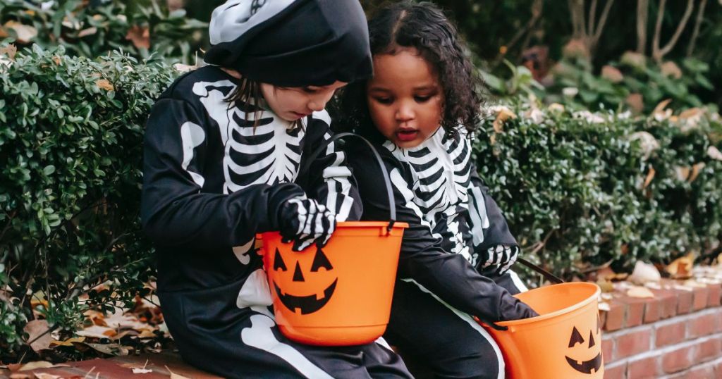 Two children dressed as skeletons sitting on a brick wall with Halloween buckets