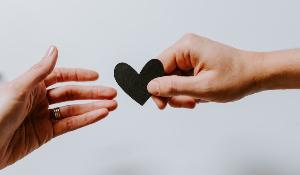 two hands reaching for black paper heart