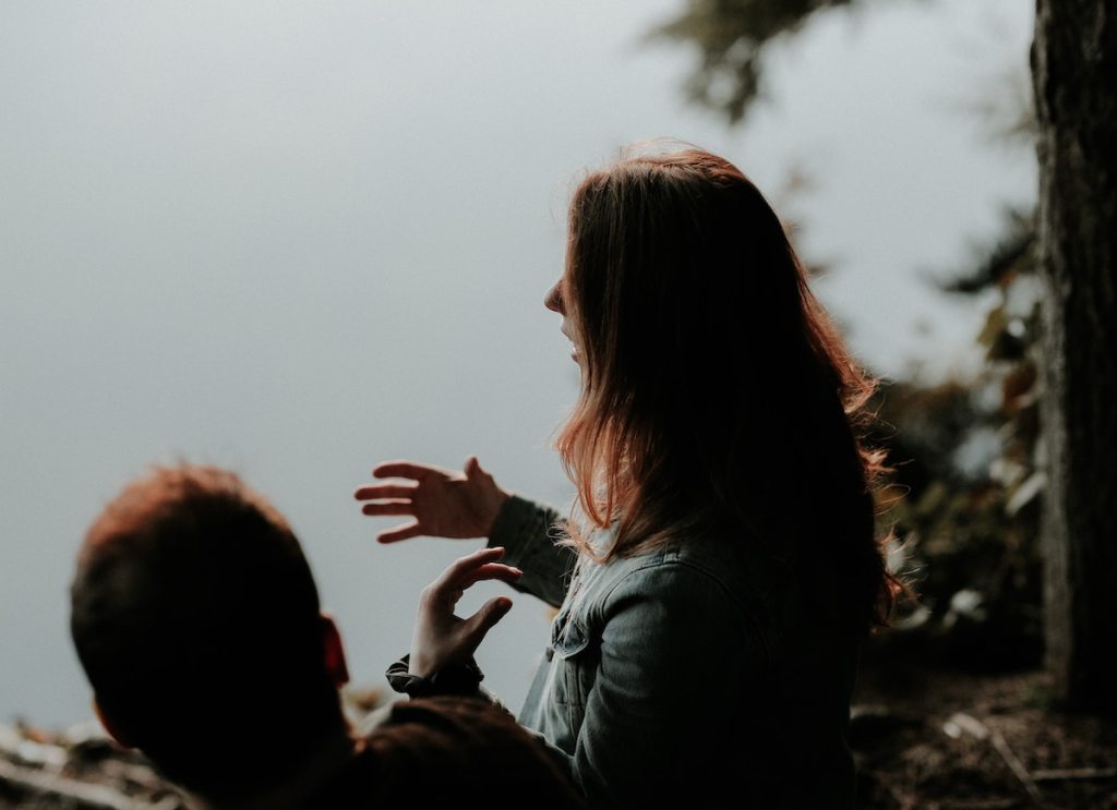 girl talking with hand gestures by lake with man 