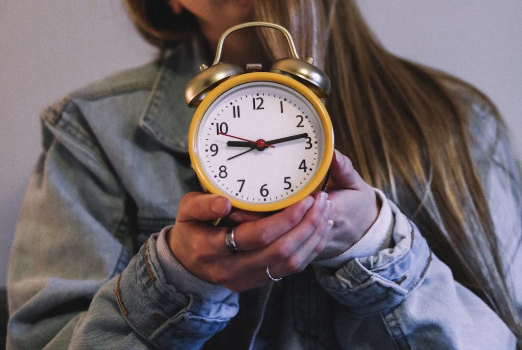 teen wearing jean jacket holding yellow alarm clock