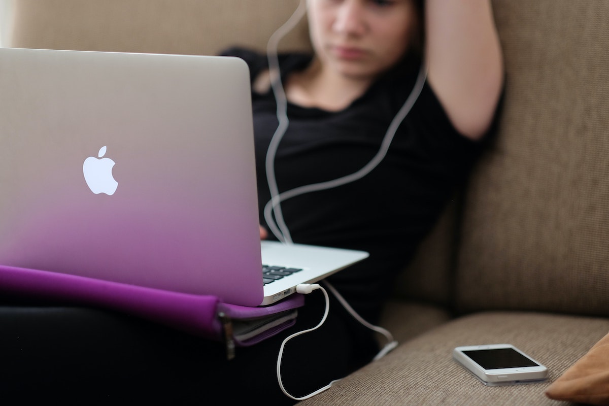 teenager sitting on couch with apple laptop on lap and phone on couch getting free internet for students 2023