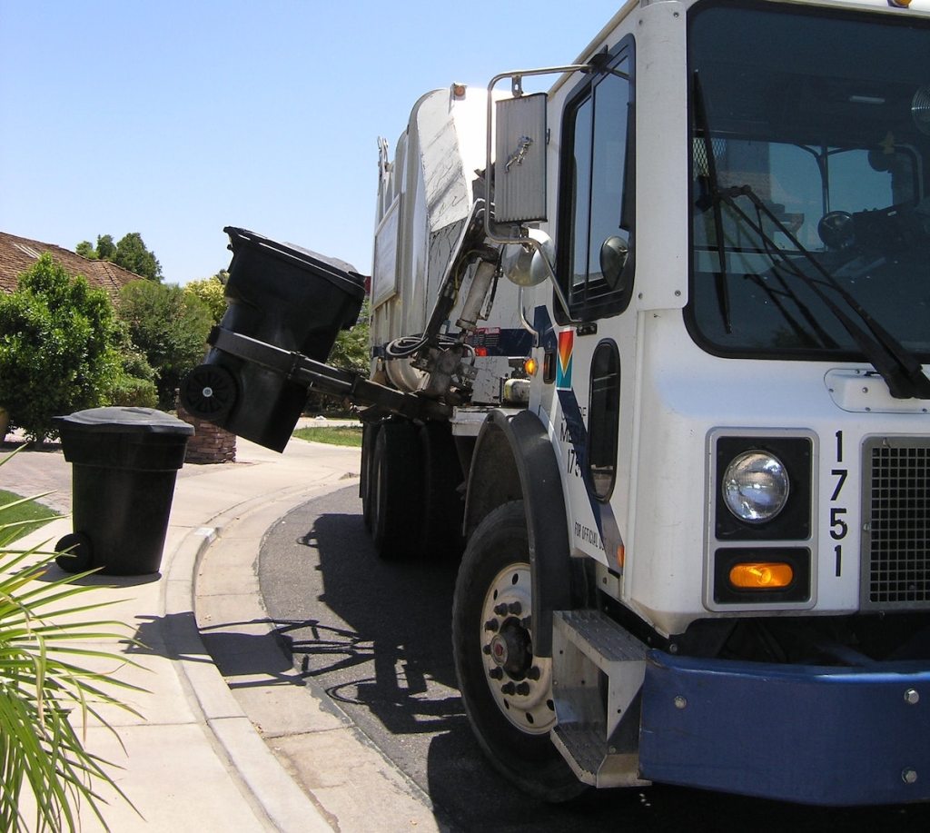 trash truck on curb picking up trash can