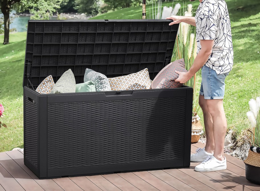 man standing next to an open outdoor deck box filled with pillows