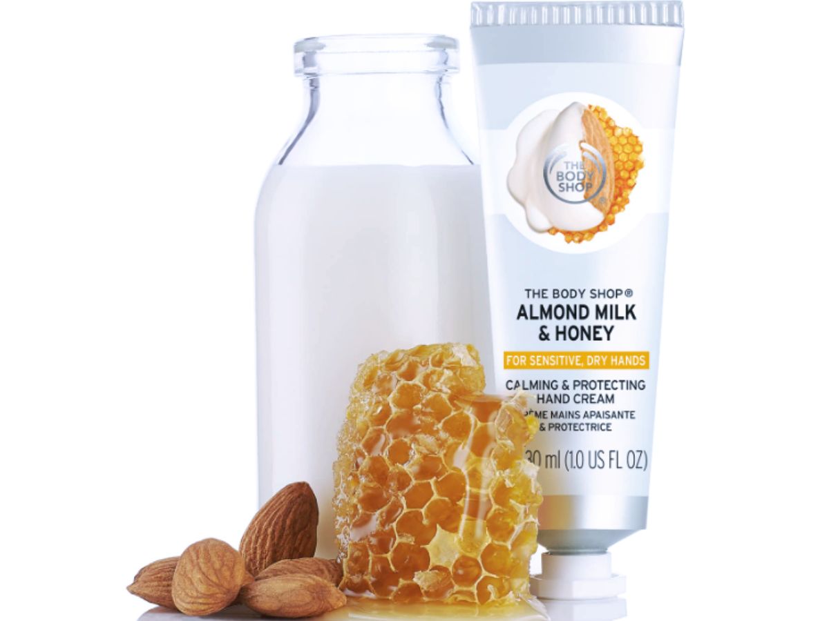 A tube of milk and honey hand cream pictured with a carafe of fresh milk, honey onlineb and almonds