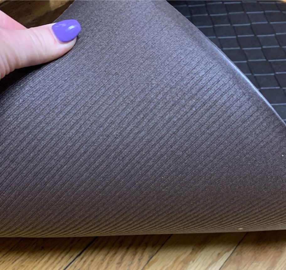 a womans hand displaying the non skid backing of a floor mat