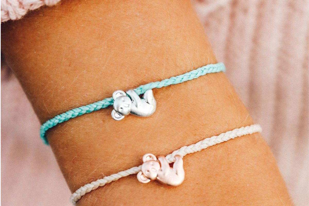 A girls wrist with 2 Pura vida Koala bear charms on bracelets.