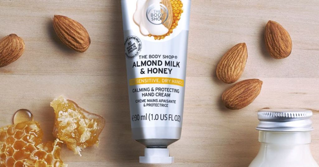 Body Shop milk and honey hand cream on a woooden counter with honeyonlineb and almonds