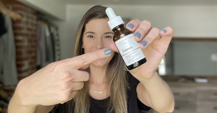 woman holding up and pointing to a bottle of The Ordinary serum