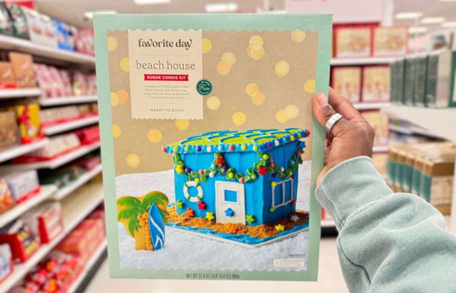 a womans hand holding a sugar cookie house decorating kit