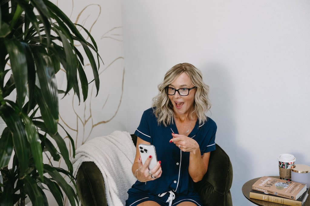 woman sitting in chair pointing to phone screen next to large plant