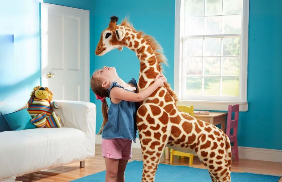 a little girl hugging a giant plush giraffe