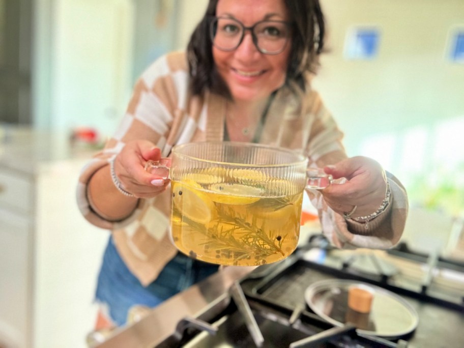 woman holding a glass pot with sliced lemons and rosemary