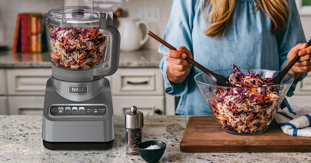 woman mixing salad bowl with the ninja chopper next to her