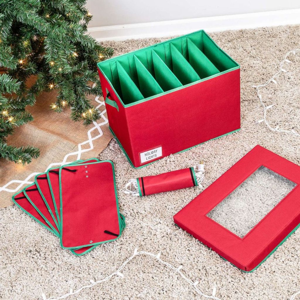 Honey-Can-Do Christmas Tree Lights Storage Box in red and green shown open and sitting by a Christmas tree