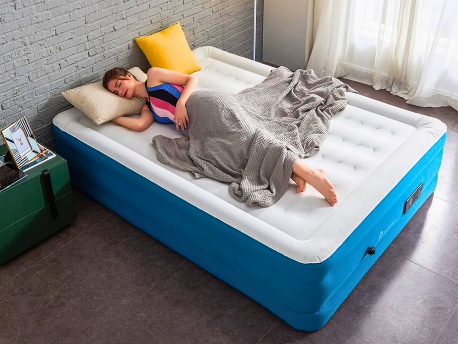 woman sleeping on a large white and blue air mattress in a bedroom