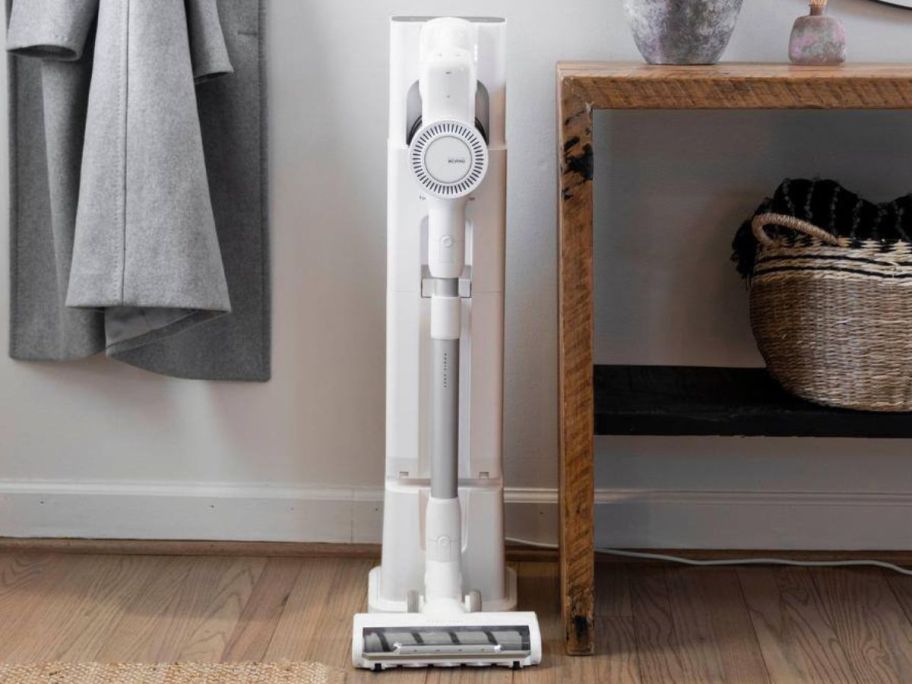 A Magic Chef Bagless Multi-Surface Cordless Stick Vacuum w/ Charging Tower next to a console table