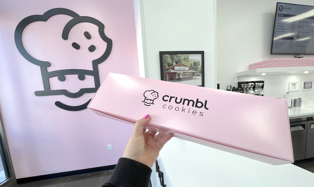 hand holding a crumbl cookies box in bakery store