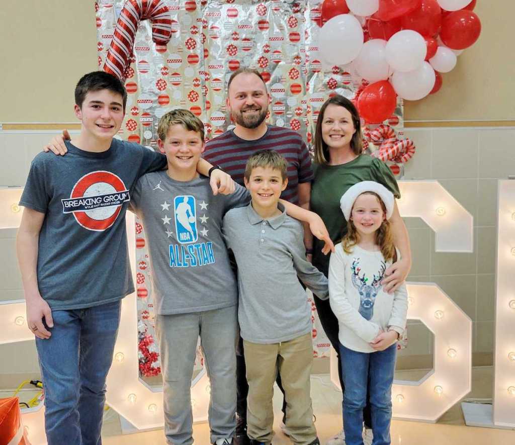 family posing in front of christmas wrapping paper and balloon backdrop