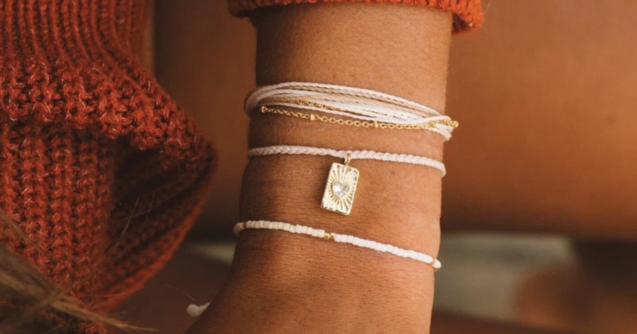 a woman's arm with a stack of string, beaded, and charm bracelets on it