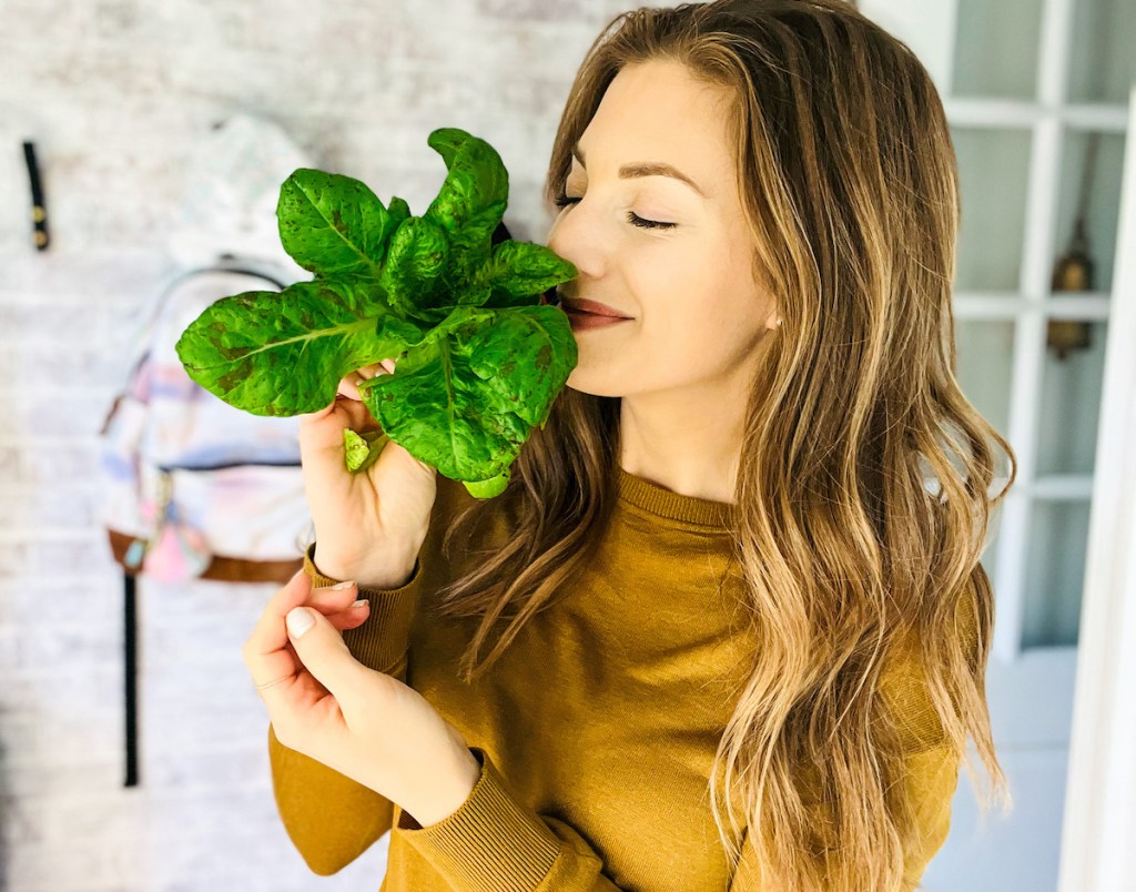 woman holding head of lettuce smelling it