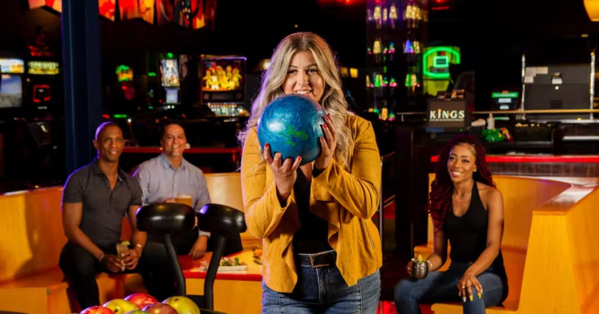 A woman holding a blue bowling ball about to bowl