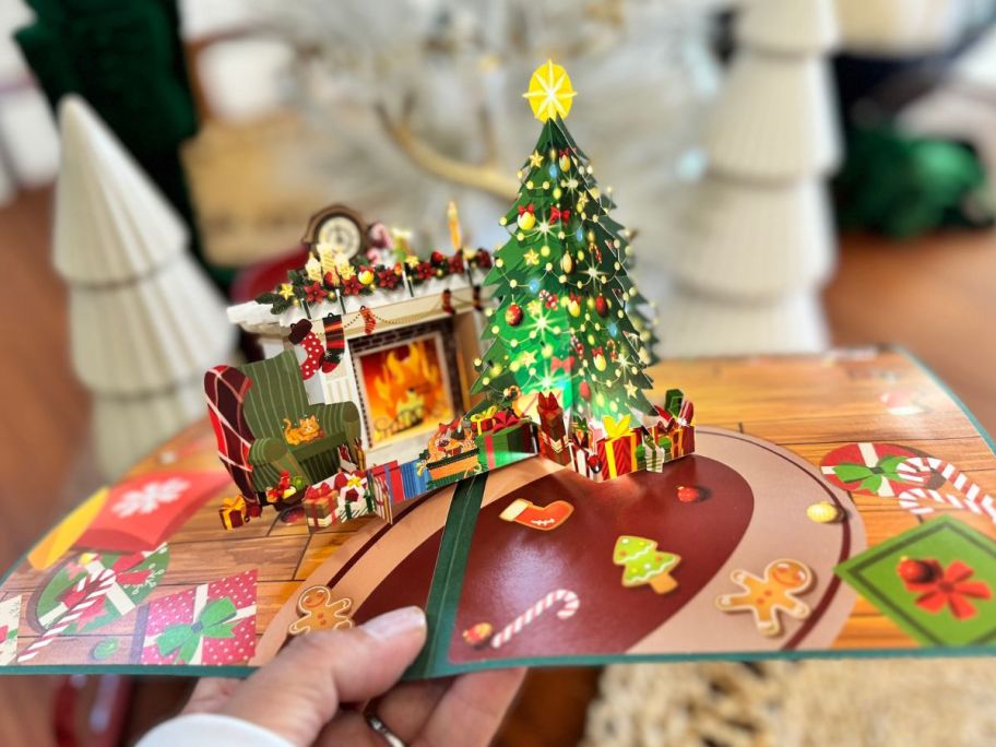 Woman holding a pop-up Christmas card with a tree and a ffireplace on it