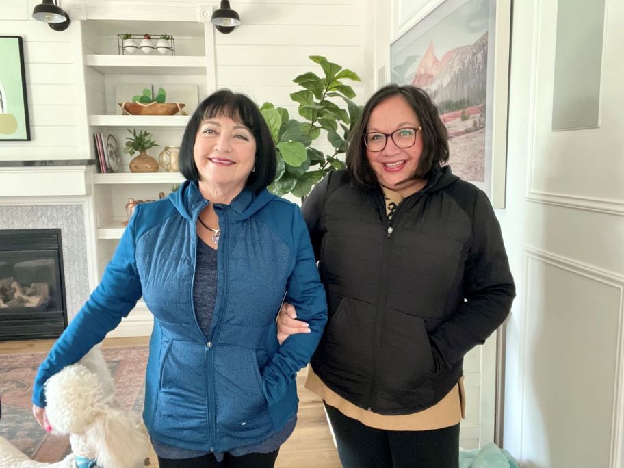 Two women standing together wearing matching jackets. One woman is in a blue jacket one is in a black jacket.