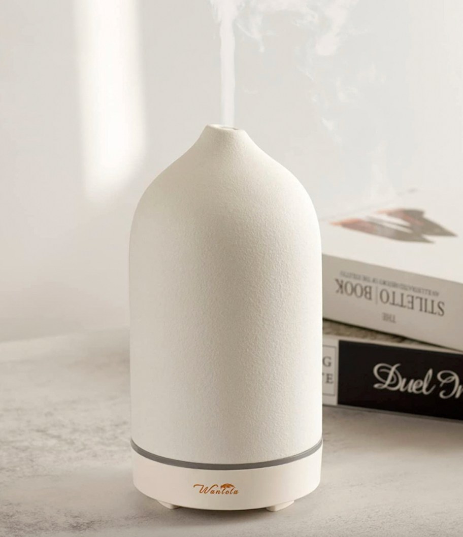 white oil diffuser sitting on table next to books 