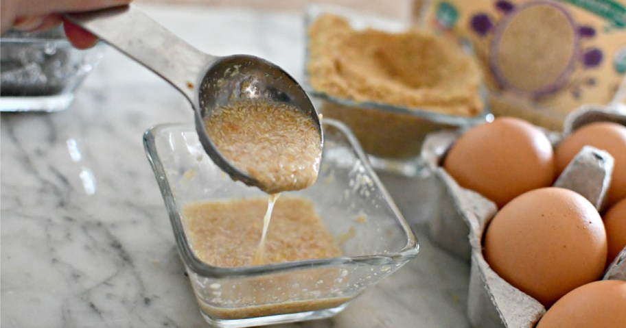 measuring spoon with liquid flax meal and carton of eggs on marble countertop