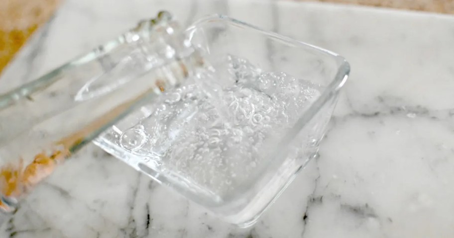 glass bottle pouring sparkling water in glass container on countertop