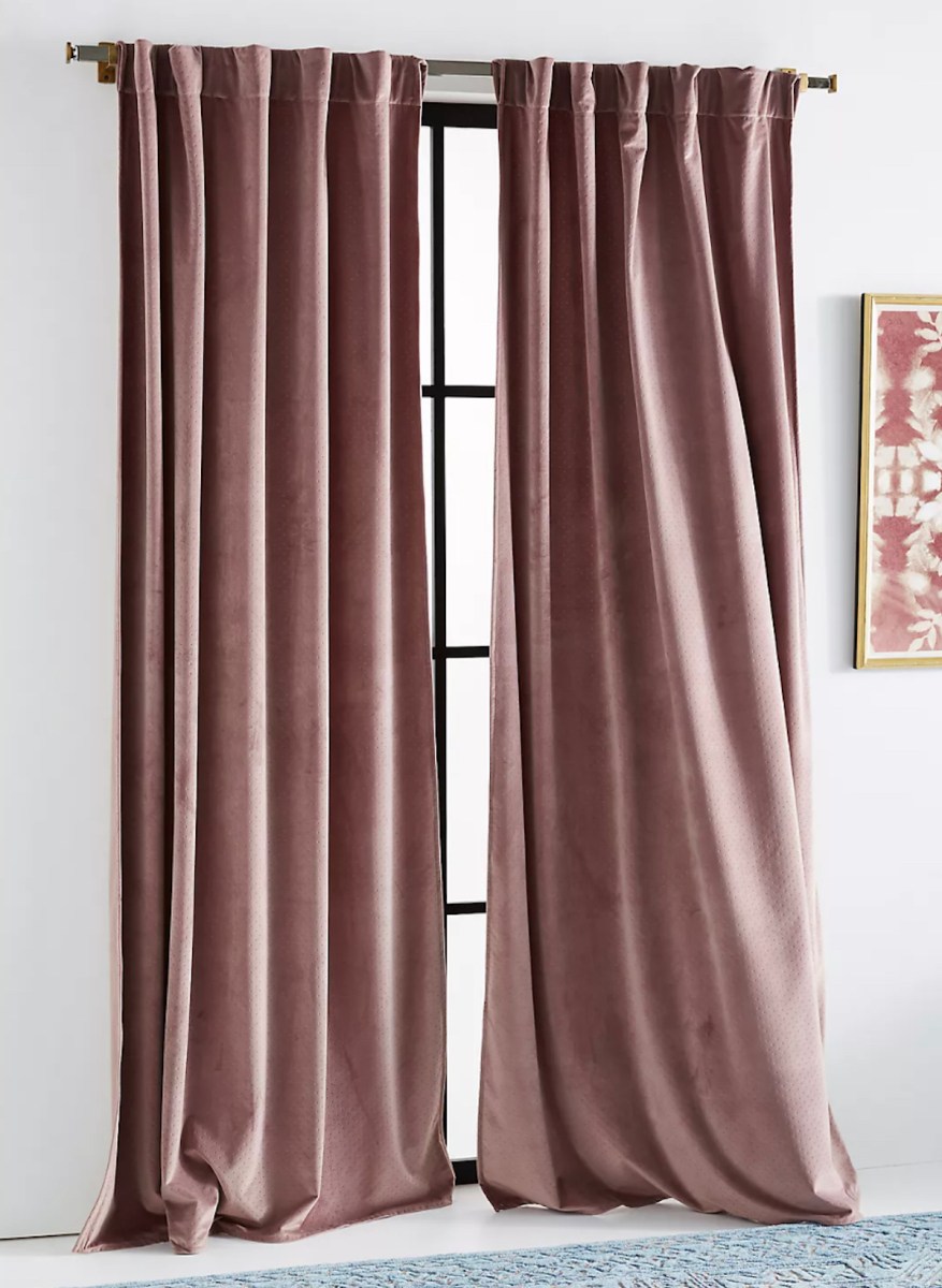 To mauve colored velvet curtains, hanging on curtain rod in front of window