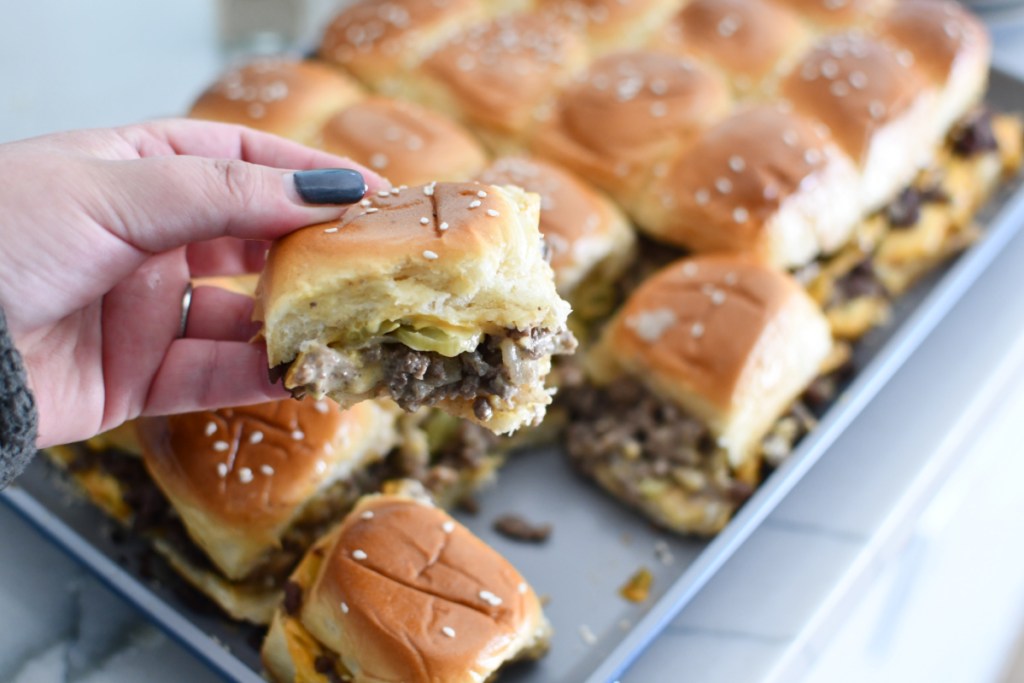 hand holding a DIY big mac slider sandwich next to a platter of sandwiches