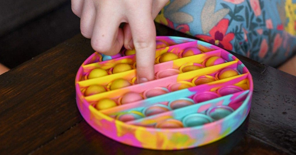 finger pushing down bubble on round pop-it toy