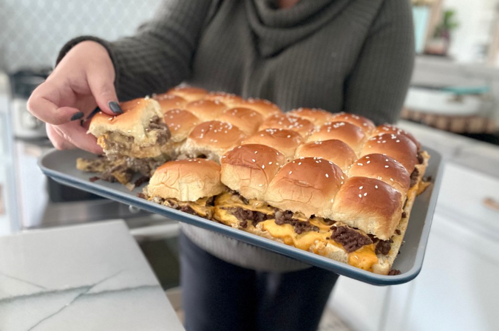 Woman holding a sheet pan of mini big mac sliders she made at home