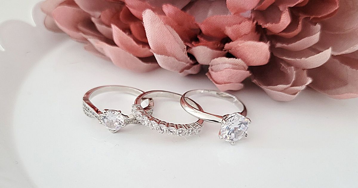 three sterling silver rings laying on decortieve white plate with pink flower in background