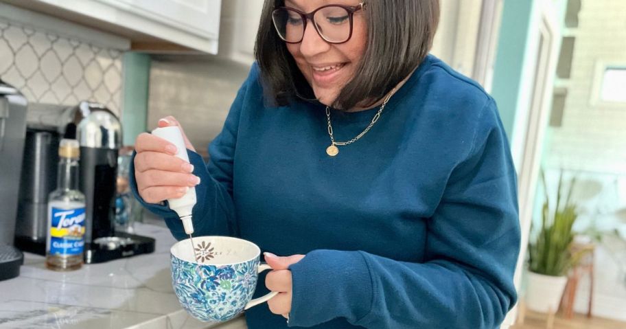 woman using a frother in her coffee cup while standing in her kitchen