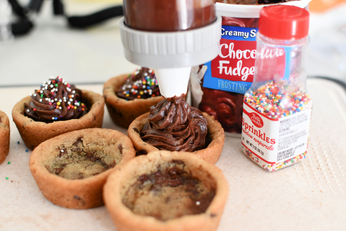 Adding chocolate frosting the top of cookies with sprinkles.