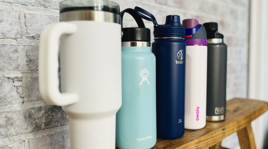 line up of different top brand water bottles on wood bench in front of brick wall